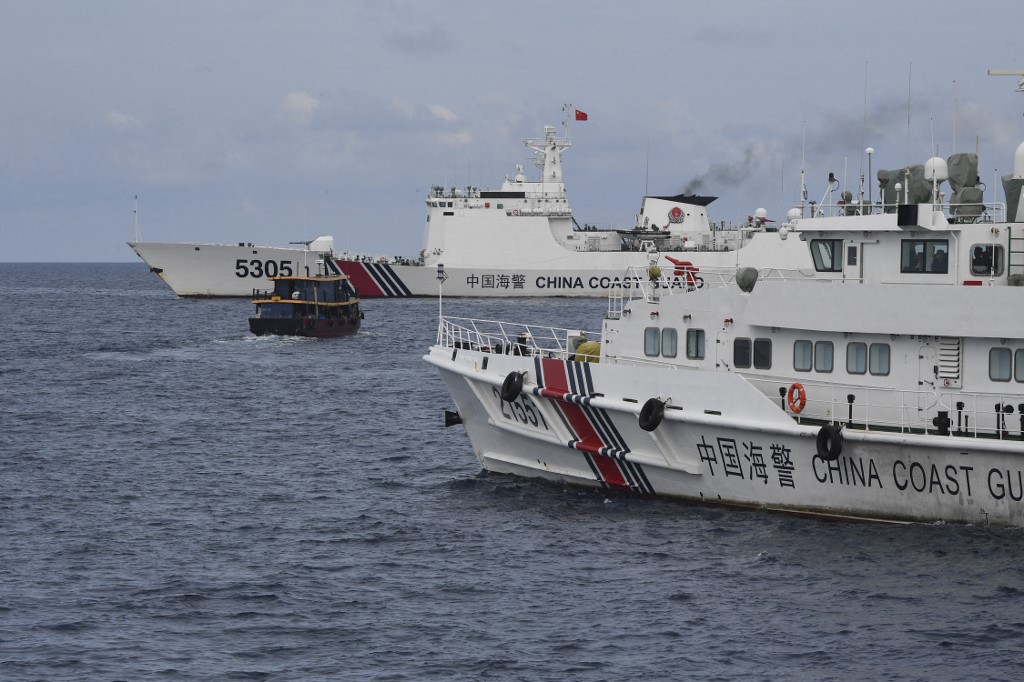 (FILES) This photo taken on August 22, 2023 shows Chinese coast guard ships (L and R) corralling a Philippine civilian boat chartered by the Philippine navy to deliver supplies to Philippine navy ship BRP Sierra Madre in the disputed South China Sea. The Philippines and China have agreed on an "arrangement" for resupplying Filipino troops stationed on a South China Sea reef, Manila said on July 21, 2024, after a series of escalatating confrontations in the disputed waters. (Photo by Ted ALJIBE / AFP)