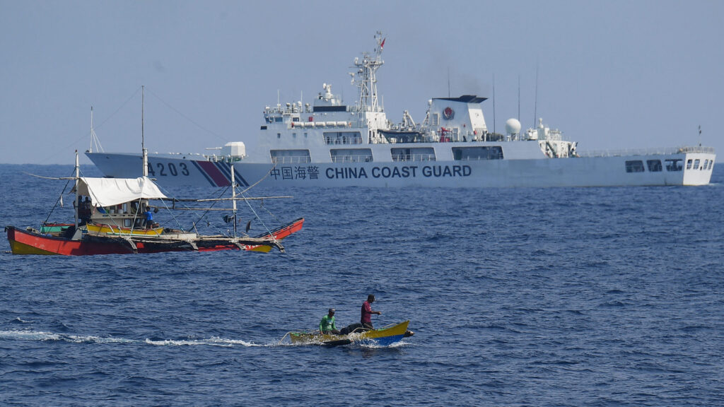 A China Coast Guard ship monitors Philippine fishermen aboard their wooden boats during the distribution of fuel and food to fishers by the civilian-led mission Atin Ito (This Is Ours) Coalition, in the disputed South China Sea on May 16, 2024. A Philippine boat convoy bearing supplies for Filipino fishers said they were headed back to port May 16, ditching plans to sail to a Beijing-held reef off the Southeast Asian country after one of their boats was "constantly shadowed" by a Chinese vessel. (Photo by Ted ALJIBE / AFP)